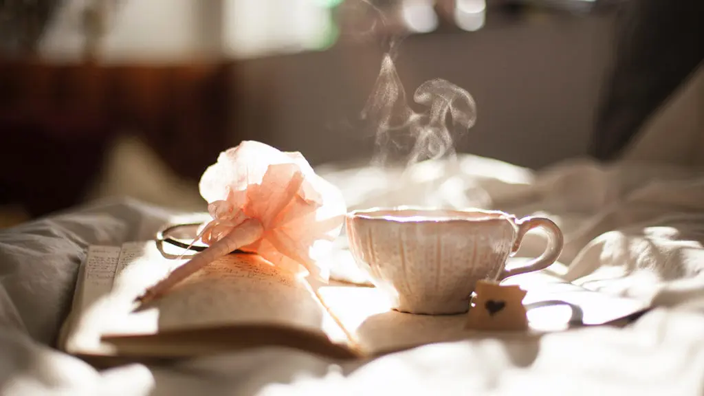 A photo of how to make tea with a cup of steaming tea on a notebook with a pen next to it.