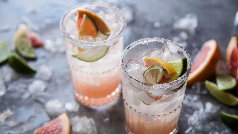 A photo of a paloma cocktail recipe with two glasses full of ice, juice, and lime wedges