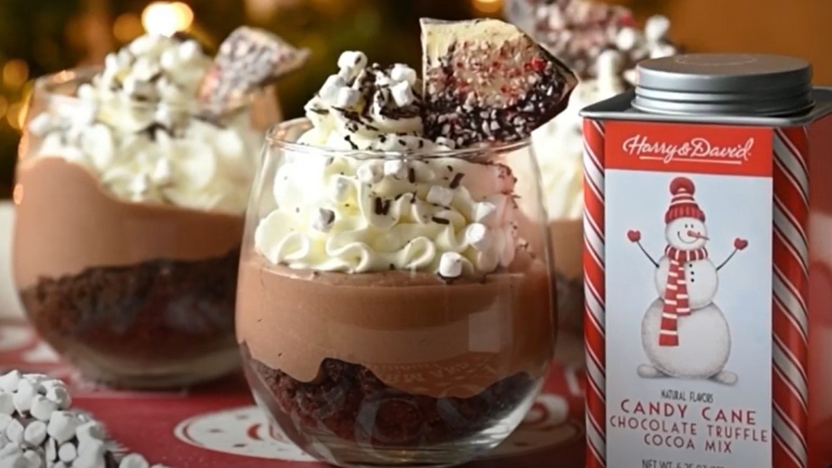 A photo of peppermint cheesecake in two trifle glasses next to a tin of peppermint hot chocolate