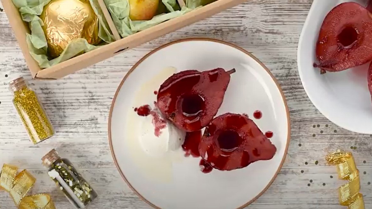 A photo of red wine poached pears on a plate surrounded by ingredients