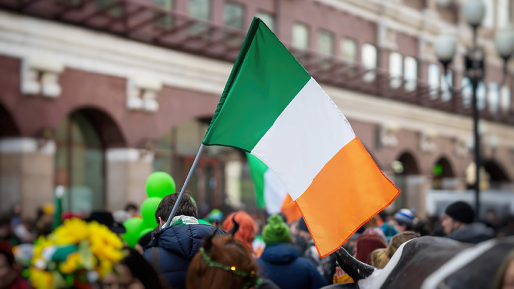 National Flag of Ireland close-up in hands of man on background of crowd people during celebration of St. Patrick's Day