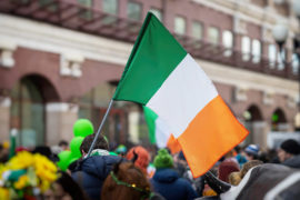 National Flag of Ireland close-up in hands of man on background of crowd people during celebration of St. Patrick's Day