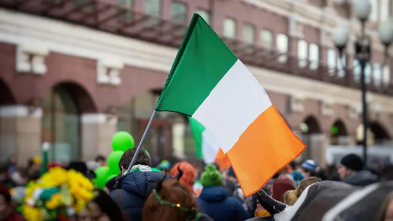 National Flag of Ireland close-up in hands of man on background of crowd people during celebration of St. Patrick's Day