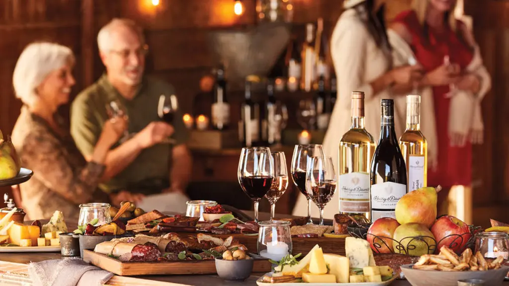 A photo of employee engagement with a table laid with charcuterie, cheese, fruit and wine with several people drinking wine in the background.