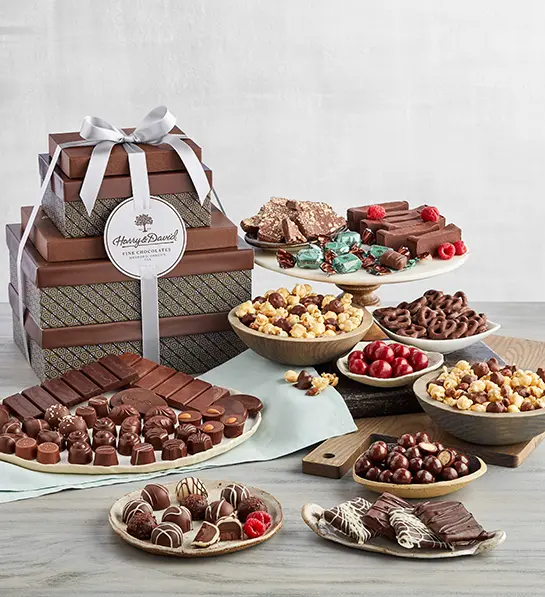 A photo of birthday gifts for sister with a collection of chocolate desserts on trays and plates next to a stack of gift-wrapped boxes.