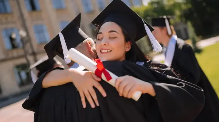 A photo of celebrations community with two graduate students hugging in graduation gowns