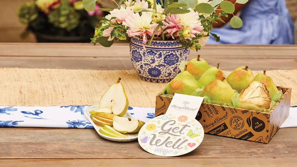 A photo of get well soon with a box of pears on a table