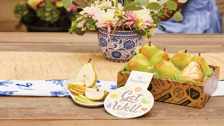 A photo of get well soon with a box of pears on a table