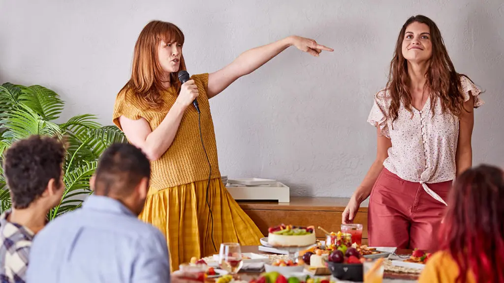 A photo of International Women's Day with two women dancing and singing at a breakfast table.