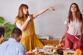A photo of International Women's Day with two women dancing and singing at a breakfast table.