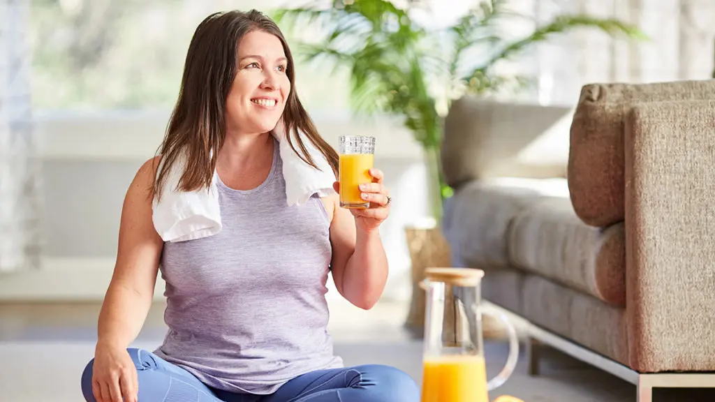A photo of employee engagement with a woman sitting on a floor drinking a glass of orange juice and smiling.