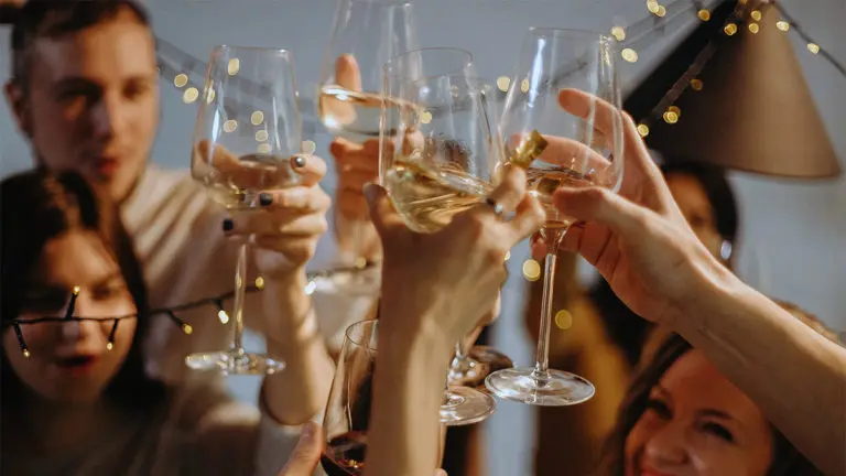 A photo of surprise birthday party with a closeup of several hands holding glasses of white wine to cheers