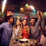 A photo of surprise birthday party with a group of people celebrating outside with roman candles