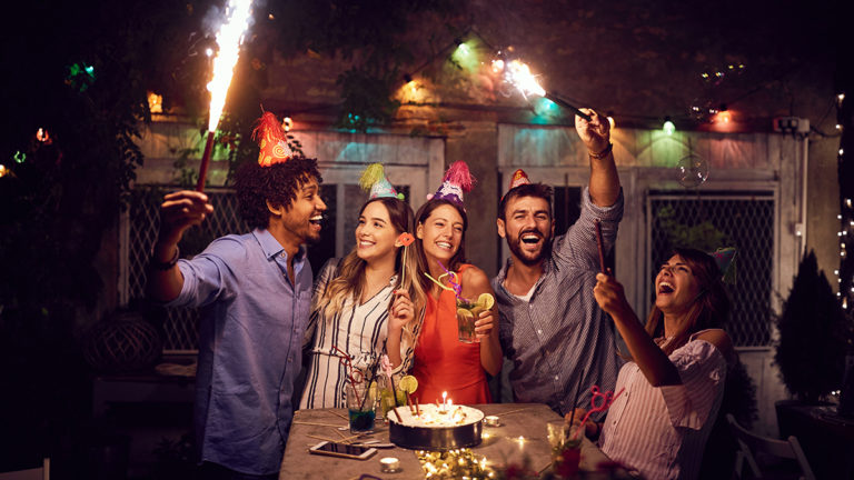 A photo of surprise birthday party with a group of people celebrating outside with roman candles