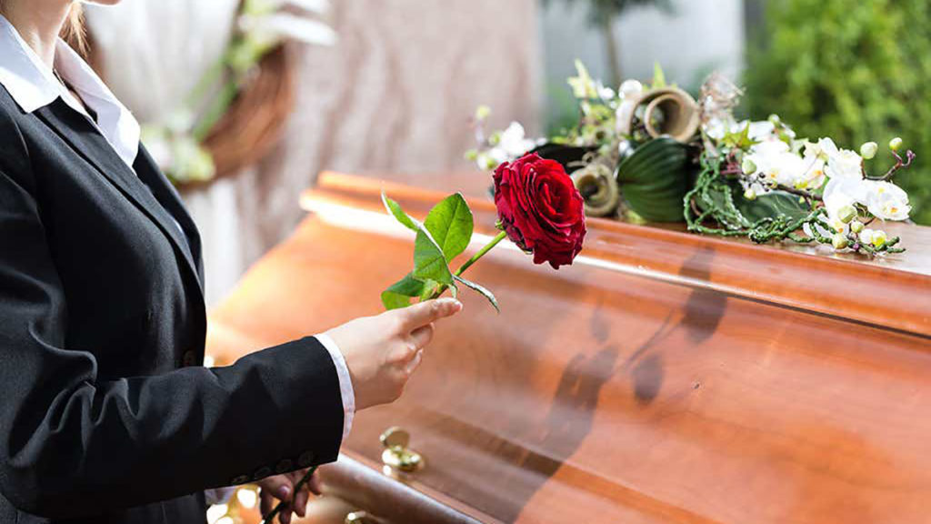 Sympathy gift etiquette with someone placing a rose on top of a casket