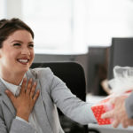 A photo of Administrative Professionals Day with a woman accepting a gift and smiling