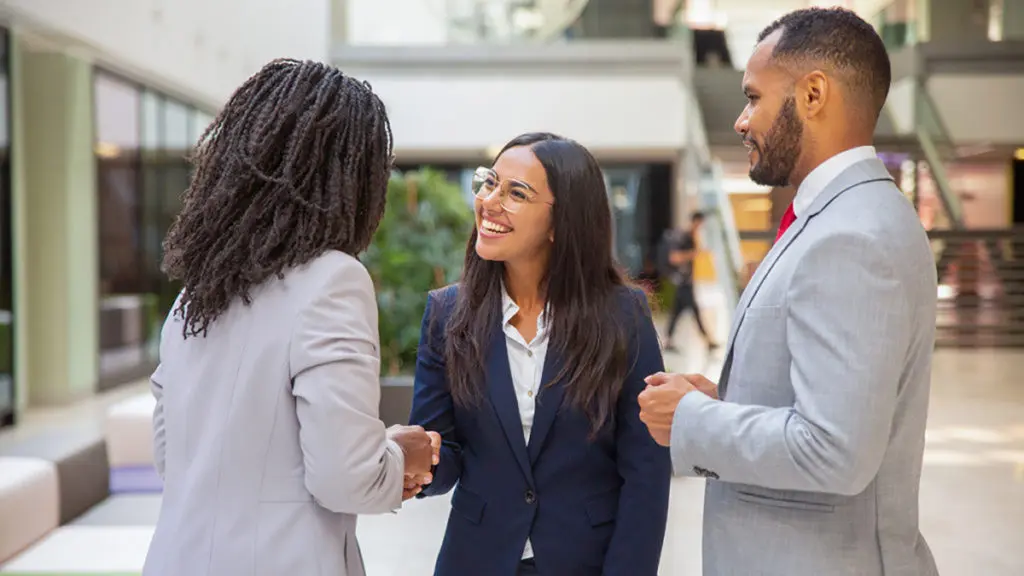 A photo of Administrative Professionals Day with three people smiling at each other and two of them shaking hands