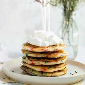 A photo of breakfast recipes with a stack of confetti pancakes topped with whipped cream