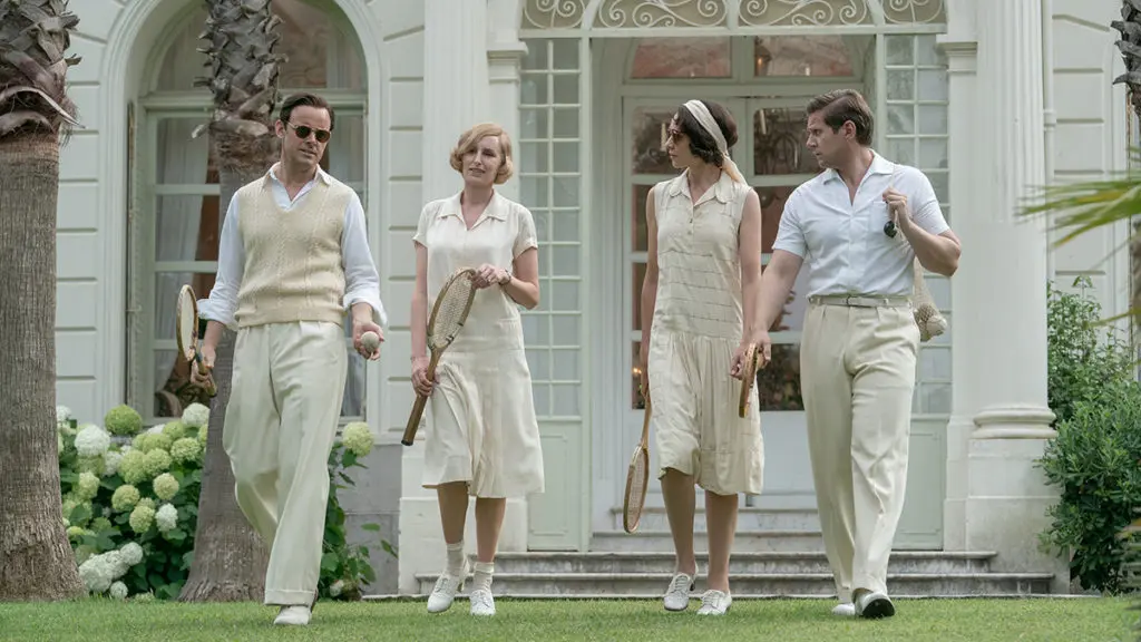 A photo of Downton Abbey party with a group of people walking on a lawn outside a large house