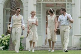 A photo of Downton Abbey party with a group of people walking on a lawn outside a large house