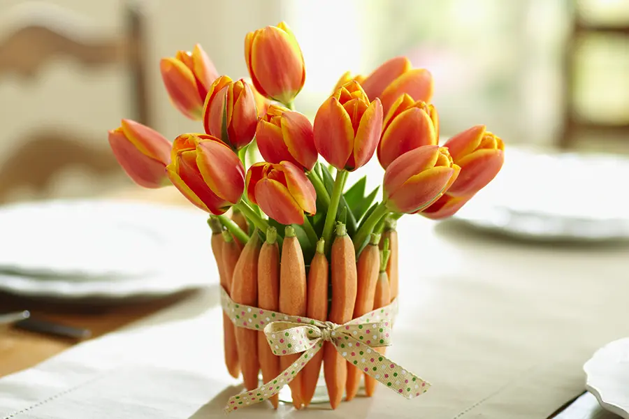 A photo of Easter brunch ideas with a bouquet of tulips on a table wrapped with a bunch of carrots