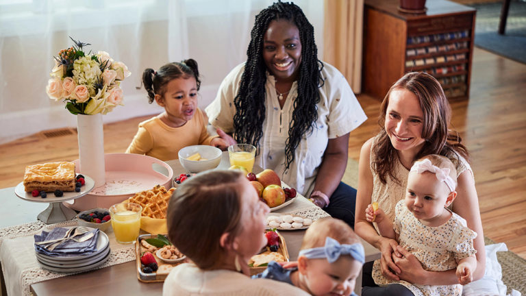 A photo of gifts for new moms with a group of women holding children sitting at a table