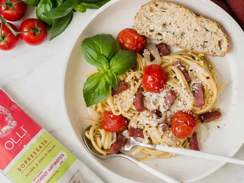 A photo of one pot pasta with salami, cherry tomatoes, and basil