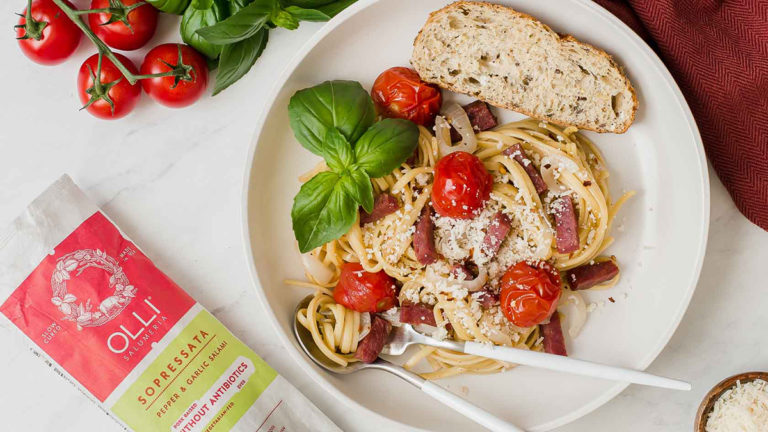 A photo of one pot pasta with salami, cherry tomatoes, and basil