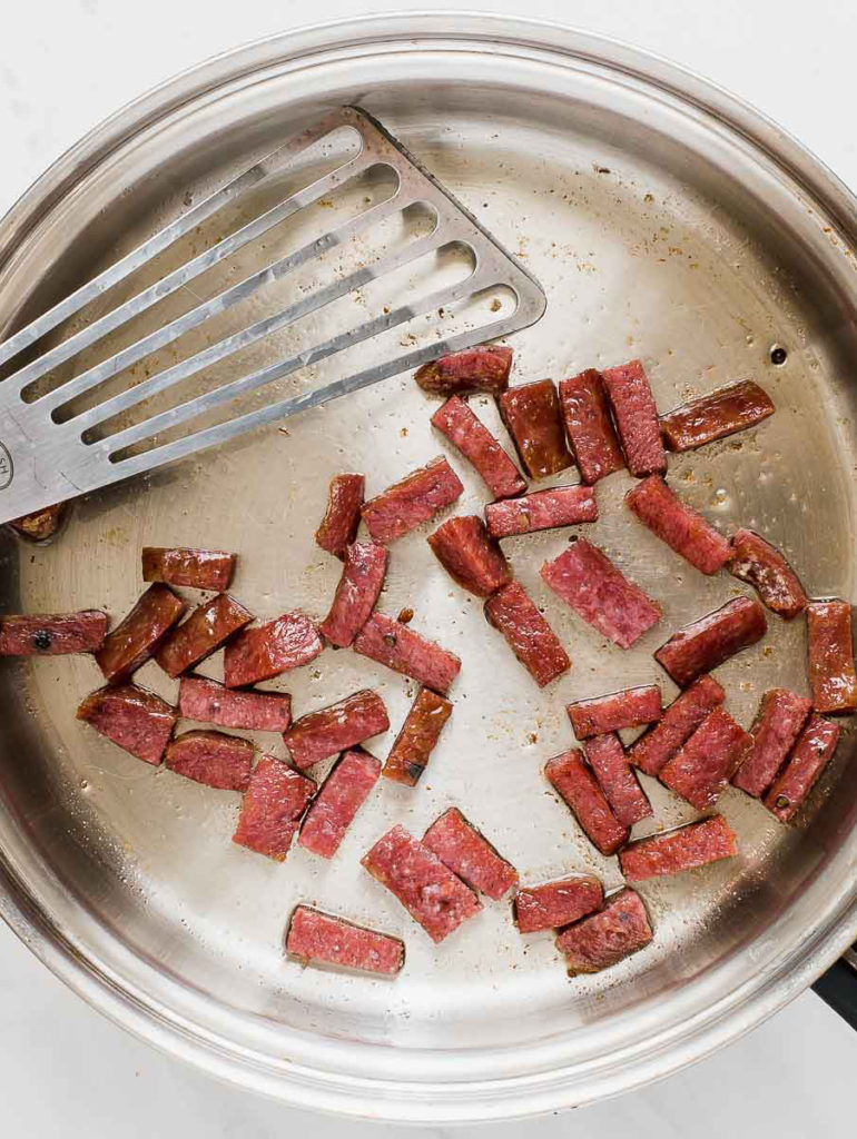 A photo of one pot pasta with a pan full of slices of salami.