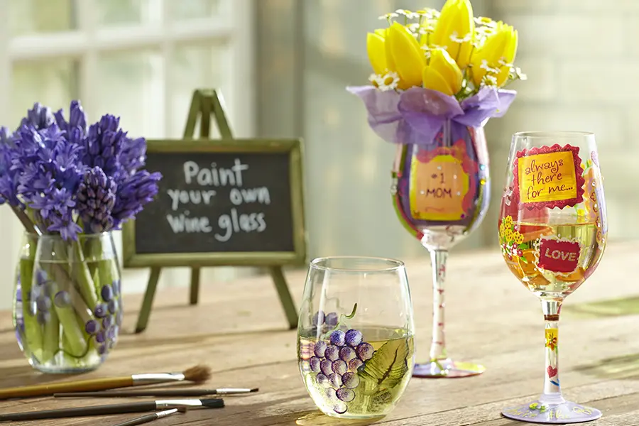 A photo of mother's day wine tasting with a bouquet of flowers next to three painted wine glasses