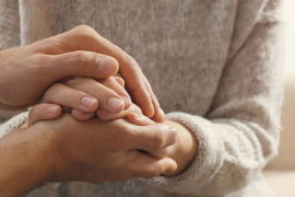 A photo of sympathy with two pairs of hands holding each other.