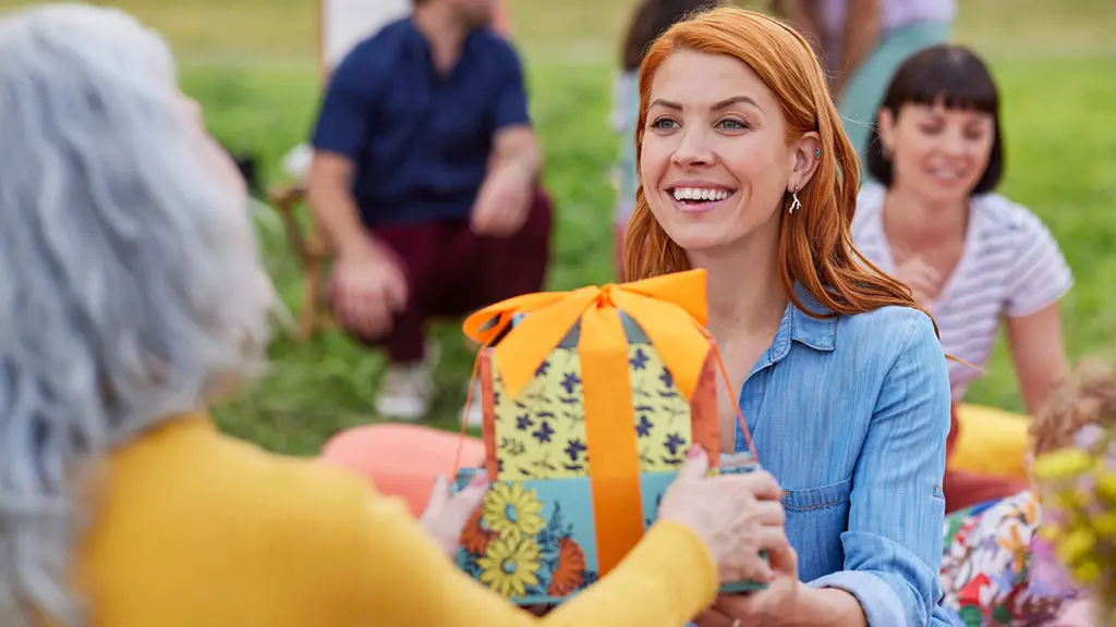 A photo of wine gifts for mom with a woman handing another woman a stack of gifts