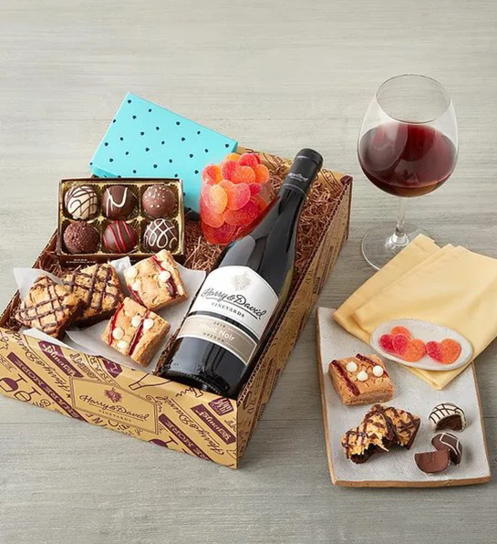 A photo of wine gifts for mom with a box of sweets with a bottle of red wine and a glass next to it