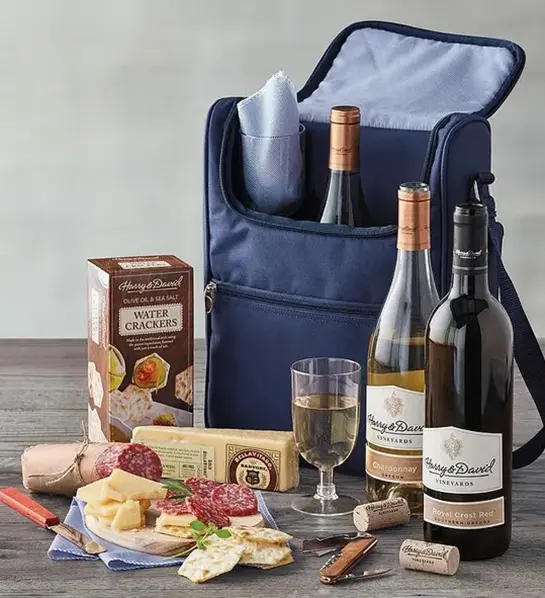 A photo of wine gifts for mom with a small cooler full of bottles of wine with charcuterie, crackers and cheese on display in front of it.
