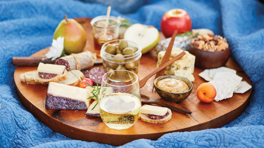 A photo of charcuterie with a spread of wine, cheese, meats, nuts and fruits on a table