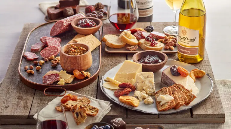 A photo of charcuterie with a table full of meats, cheese, nuts, wine and other snacks