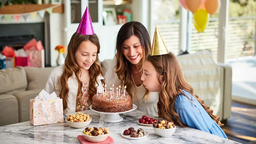 A photo of june birthdays with two girls blowing out the candles on a cake surrounded by their mom and chocolate treats