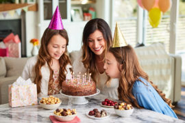 A photo of june birthdays with two girls blowing out the candles on a cake surrounded by their mom and chocolate treats