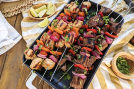 A photo of kebabs with a tray of steak and chicken kebabs on a table