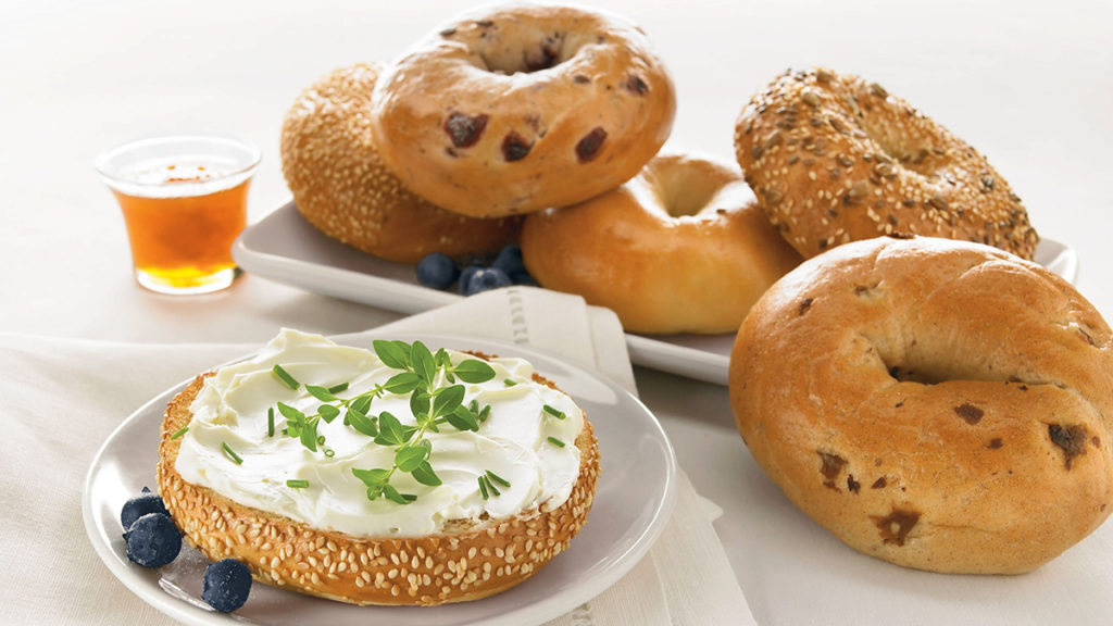 A photo of origin of the bagel with a bagel smeared with cream cheese and several whole bagels next to it.