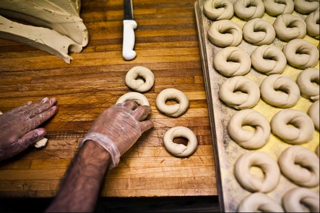 A photo of origin of the bagel with someone hand rolling dough into bagel shapes