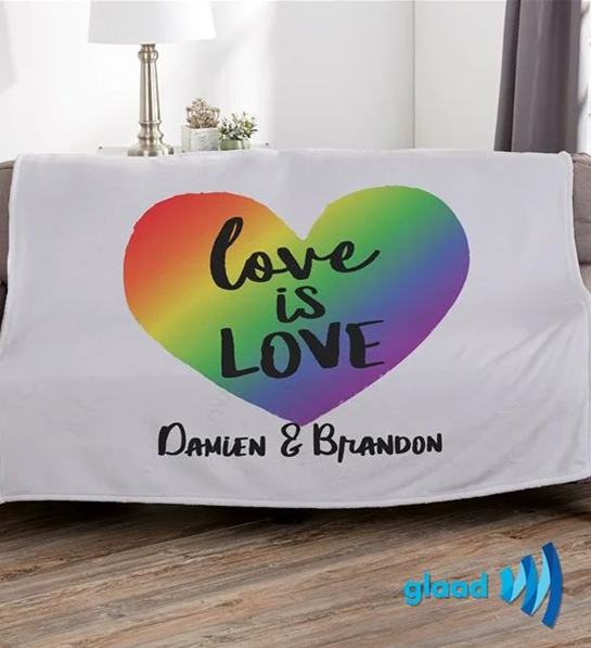A photo of pride month gifts with a personalized blanket with a rainbow heart with the words "love is love" inside it
