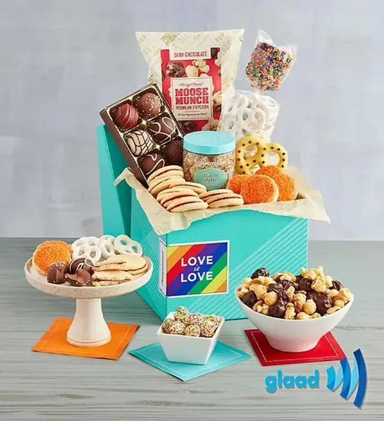 A photo of pride month gifts with a box full of chocolate, cookies, popcorn and other treats surrounded by the same items.