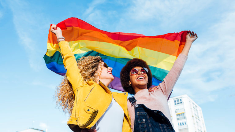 A photo of pride month gifts with two women holding a pride flag