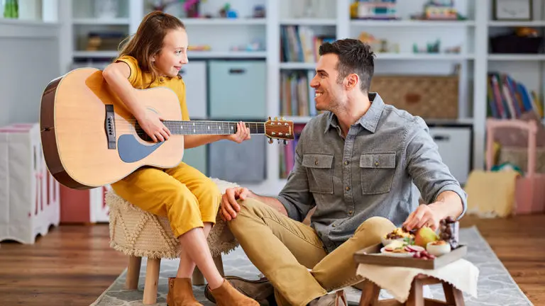 A photo of celebrate father's day with a young girl playing guitar with her father next to her