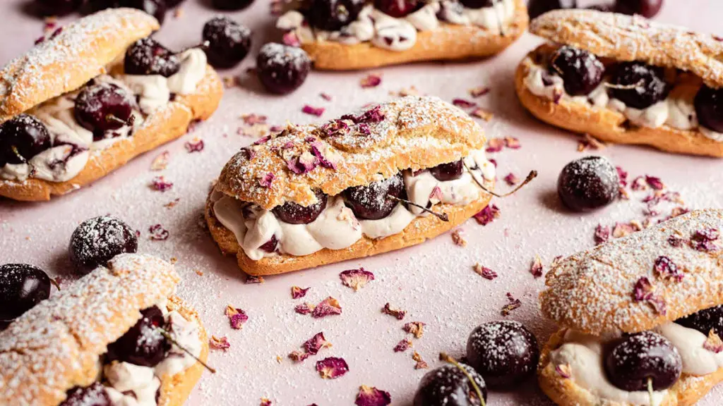 Photo of an eclair surrounded by several more all filled with cream and cherries