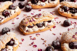 Photo of an eclair surrounded by several more all filled with cream and cherries