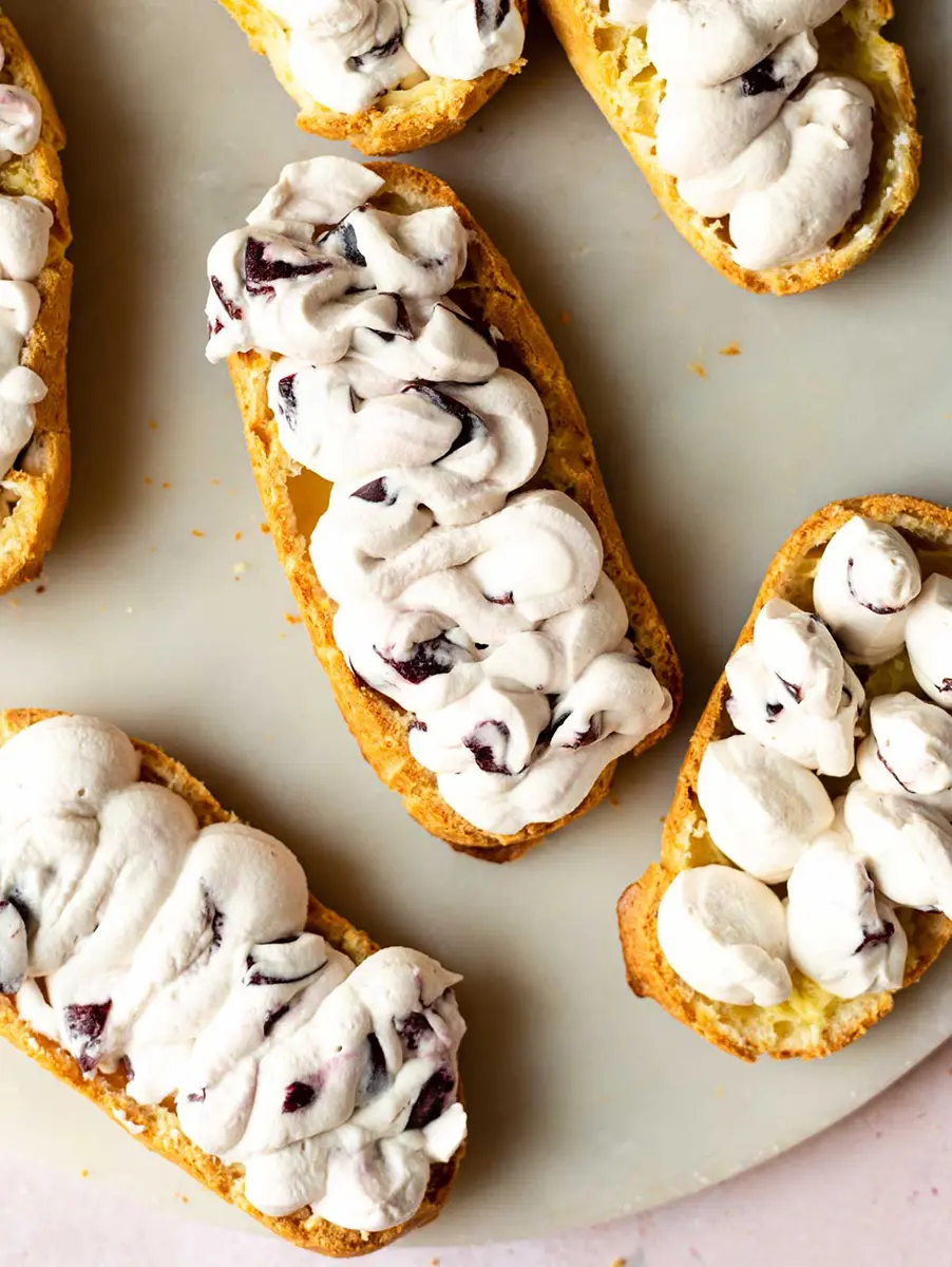 Photo of eclair bottoms topped with cream full of cherries.