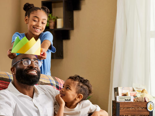 A photo of father's day gift guide with two kids putting a paper crown on their dad's head