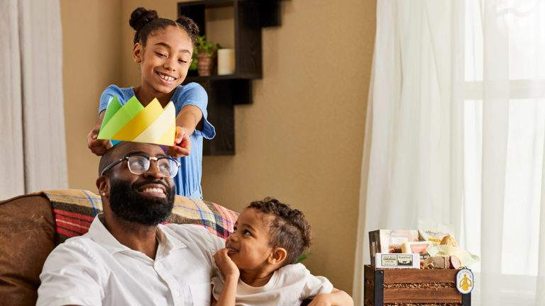 A photo of father's day gift guide with two kids putting a paper crown on their dad's head